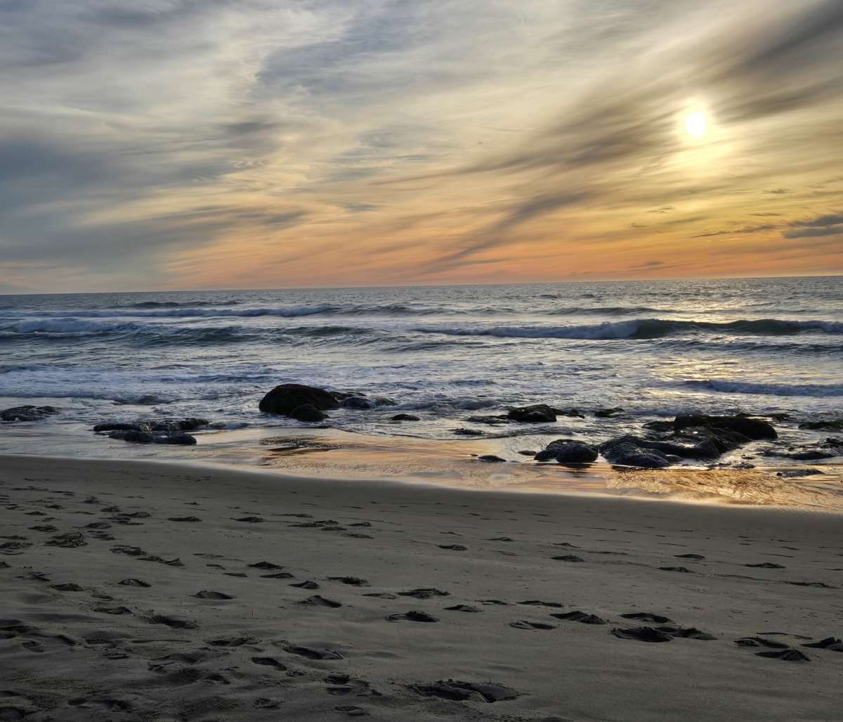 Sunset over breaking waves and rocks along the beach.