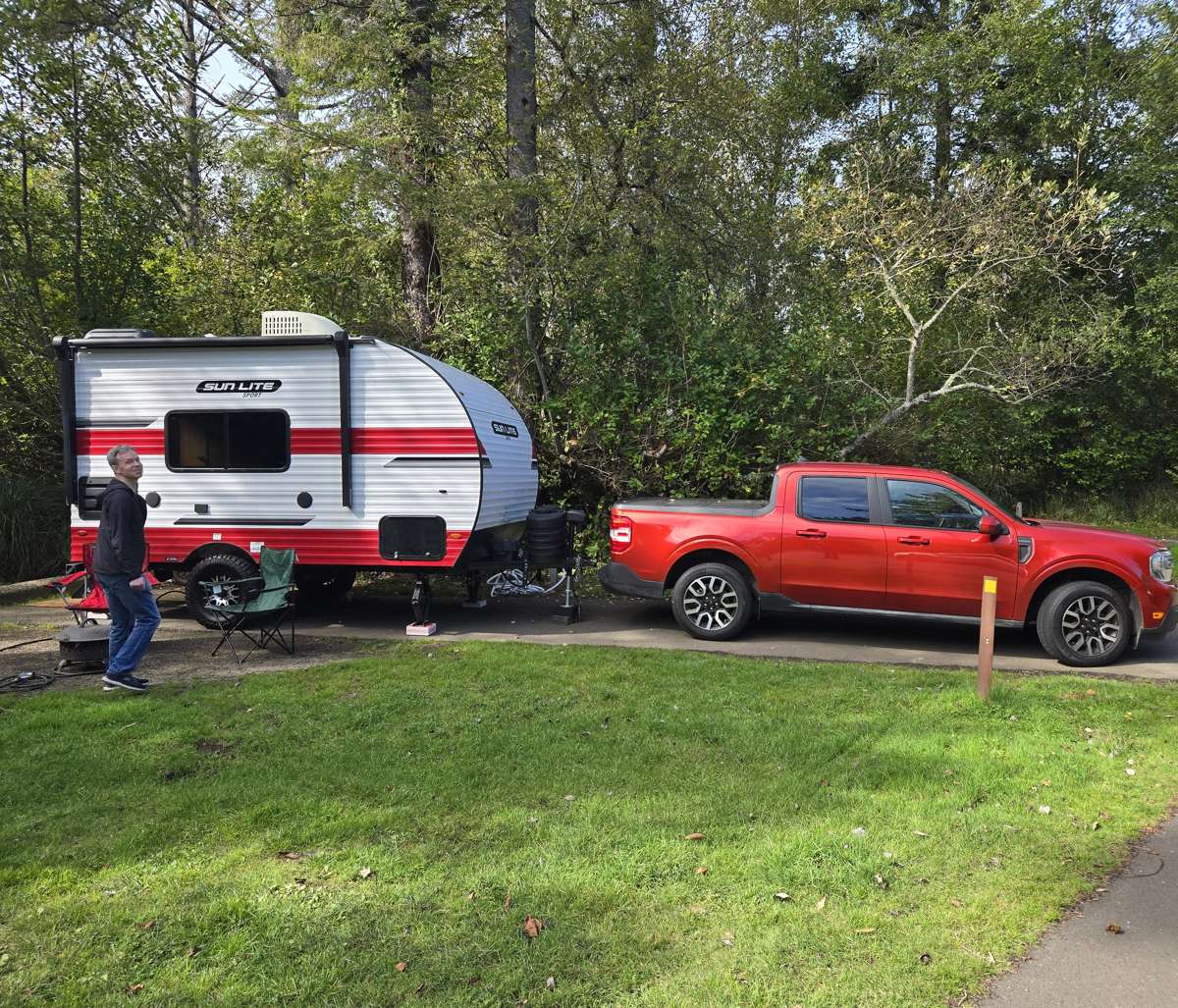Red pickup truck and red-and-white camping trailer at a wooded campsite.