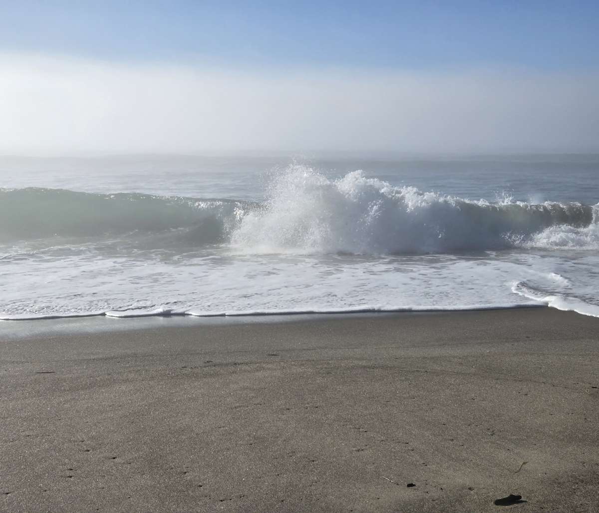 A wave curling and breaking toward the sandy beach.