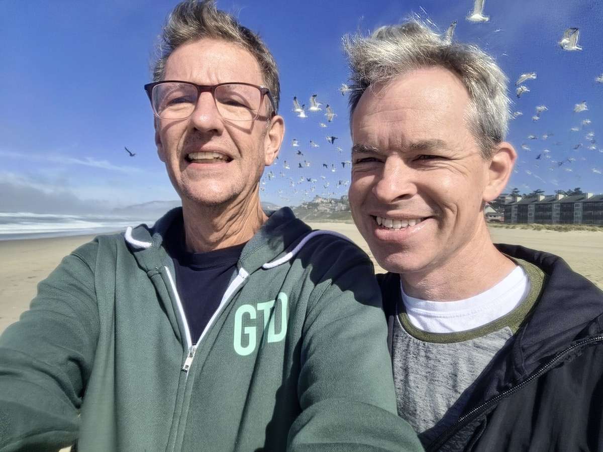 Peter B Dowell and Justin Jones smiling together on a sunny beach.